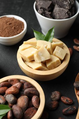 Organik kakao yağı, fasulye, çikolata parçaları, toz ve yeşil yapraklar siyah masada, yakın plan.