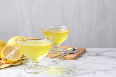 Tatlı kaselerinde leziz sarı jöle ve beyaz mermer masada taze limonlar, yakın plan. Metin için boşluk