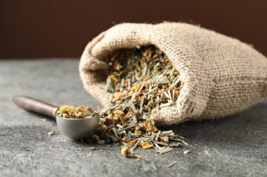 Torbada kurutulmuş bitki çayı ve gri masada ölçü kaşığı, yakın plan.