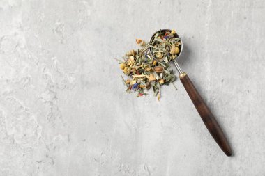 Açık gri masada kurutulmuş bitki çayı ve ölçü kaşığı, üst manzara. Metin için boşluk