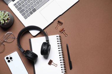 Kulaklıklar, dizüstü bilgisayarlar, akıllı telefonlar, gözlükler, kırtasiye malzemeleri ve kahverengi arka planda çiçek dekoru, düz uzanma