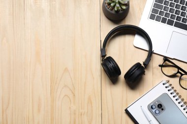 Kulaklıklar, akıllı telefon, bilgisayar klavyesi, gözlükler, kırtasiye malzemeleri ve ahşap masa üzerindeki çiçek dekoru, düz yatak. Metin için boşluk