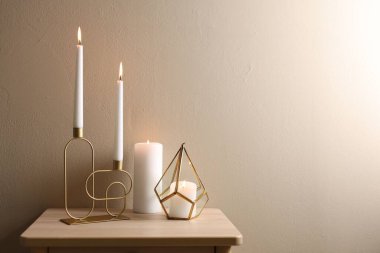 Bej duvarın yanındaki ahşap masada şamdanların içinde yanan mumlar. Metin için boşluk
