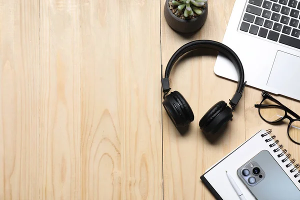 Kulaklıklar, akıllı telefon, bilgisayar klavyesi, gözlükler, kırtasiye malzemeleri ve ahşap masa üzerindeki çiçek dekoru, düz yatak. Metin için boşluk