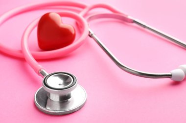 Pembe arka planda steteskop ve kırmızı kalp, yakın plan.