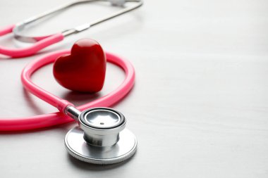 Pembe steteskop ve kalp modeli açık tahta masada, yakın plan. Metin için boşluk