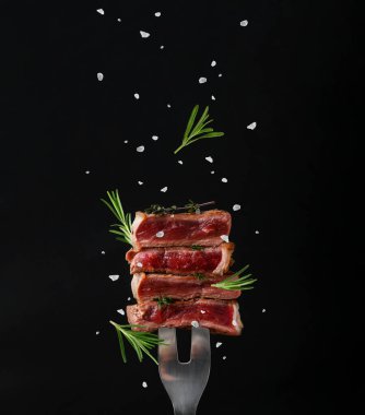 Et çatalı, kekik, biberiye ve tuz üzerine sığır eti parçaları siyah arkaplanda