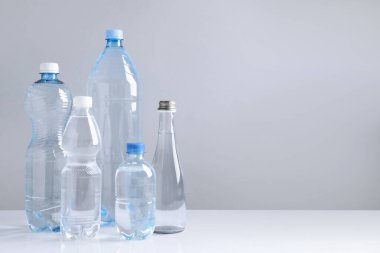 Beyaz masada gri arkaplan ile farklı boyutlarda su şişeleri, metin için boşluk
