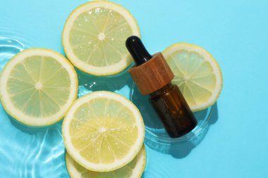 Bir şişe kozmetik ürünü ve limon dilimleri açık mavi arka planda, düz yerde.