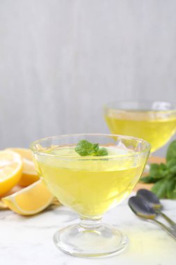 Tatlı kaselerinde leziz sarı jöle, beyaz mermer masada taze limon, yakın plan.