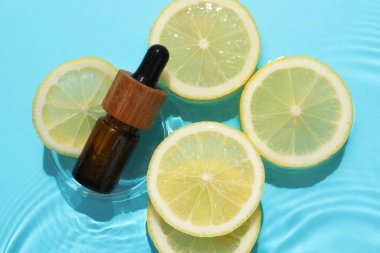 Bir şişe kozmetik ürünü ve limon dilimleri açık mavi arka planda, düz yerde.
