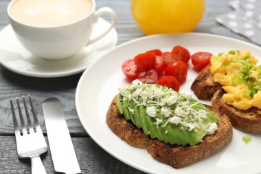 Gri ahşap masada servis edilen lezzetli avokado tostlu sağlıklı bir kahvaltı.
