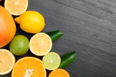 Farklı taze narenciye meyveleri ve yeşil yapraklar siyah masada, düz yerde. Metin için boşluk