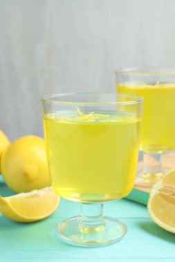 Tatlı kaselerinde leziz sarı jöle ve açık mavi ahşap masada limonlar, yakın plan.