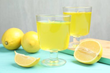 Tatlı kaselerinde leziz sarı jöle ve açık mavi ahşap masada limonlar, yakın plan.