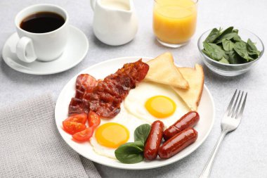 Açık gri masada servis edilen kızarmış yumurta, sosis ve pastırma ile nefis bir kahvaltı.