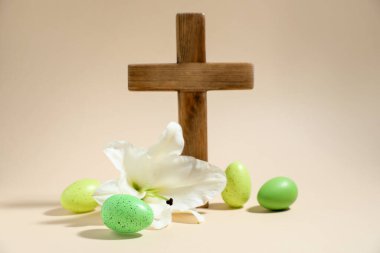 Paskalya. Ahşap haç, boyalı yumurta ve bej arka planda güzel zambak çiçeği, yakın plan.