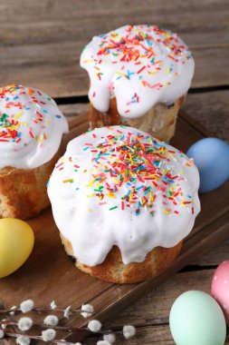 Lezzetli Paskalya pastaları, boyanmış yumurtalar ve söğüt dalları ahşap masada, yakın plan.