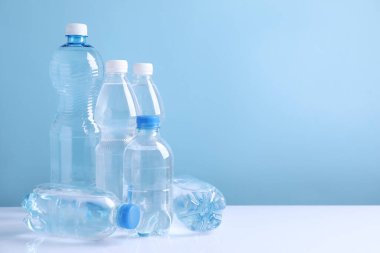 Beyaz masada açık mavi arka planda farklı boyutlarda su şişeleri var. Metin için boşluk