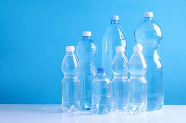 Açık mavi arka planda beyaz masada farklı boyutlarda su şişeleri