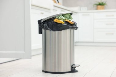 Mutfakta yerde çöp dolu metal çöp kovası.