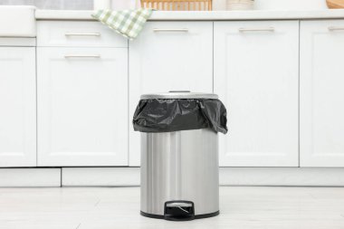 Mutfakta yerde plastik torba olan metal çöp kutusu.