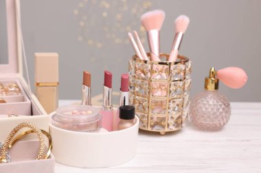 Makyaj ürünleri tutacaklarda ve mücevher kutusu açık ahşap masada gri arka planda, yakın plan. Bokeh etkisi