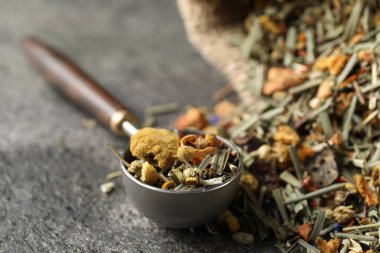 Torbada kurutulmuş bitki çayı ve gri masada ölçü kaşığı, yakın plan.