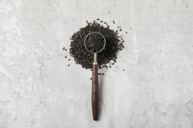 Kurumuş siyah çay yaprakları ve açık gri masada kaşık ölçüsü.