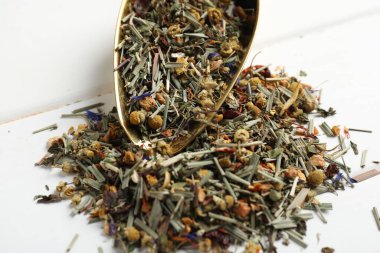 Beyaz ahşap masada kurutulmuş bitki çayı ve metal spatula, yakın plan.