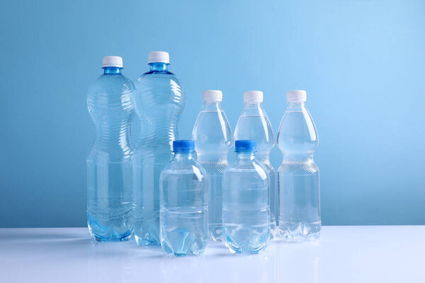 Water bottles of different sizes on white table against light blue background