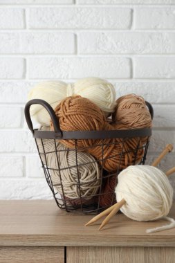 Beyaz tuğla duvarın yanındaki ahşap masada iplikler ve iğneler var.