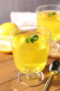 Tatlı kaselerinde leziz sarı jöle, nane ve taze limon ahşap masada, yakın plan.