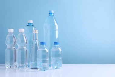 Beyaz masada açık mavi arka planda farklı boyutlarda su şişeleri var. Metin için boşluk