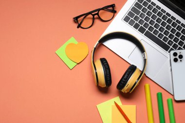 Kulaklık, dizüstü bilgisayar, akıllı telefon, mercan arka planda gözlük ve kırtasiye malzemesi. Metin için boşluk