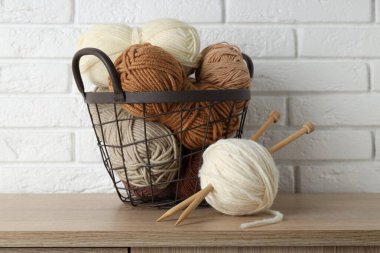 Örgü iplikleri ve iğneler beyaz tuğla duvarın yanındaki ahşap masada, yakın plan.