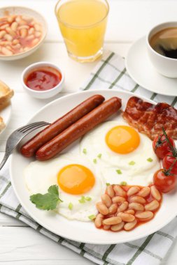Geleneksel İngiliz kahvaltısı. Lezzetli, güneşli, pastırmalı yumurta ve sosisler beyaz ahşap masada servis ediliyor, yakın plan.