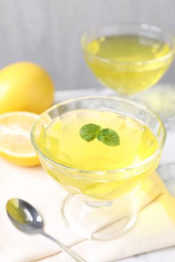 Tatlı kaselerinde leziz sarı jöle, masada nane ve taze limon, yakın plan.
