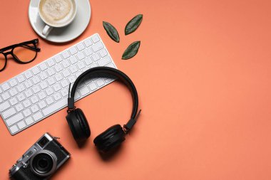 Headphones, computer keyboard, smartphone, vintage camera, coffee, glasses and leaves on coral background, flat lay. Space for text