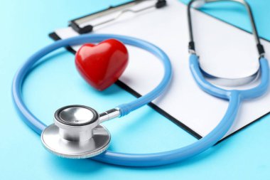Stetoskop, kalp modeli ve açık mavi arkaplanda pano, yakın plan