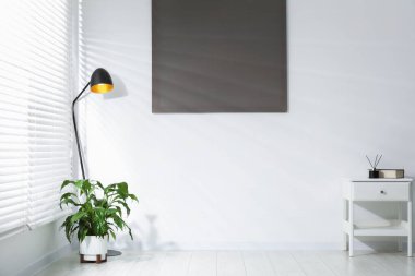 Havalı lamba, ev bitkisi ve şifonyer beyaz duvarın yanında, yazı için yer var. İç tasarım