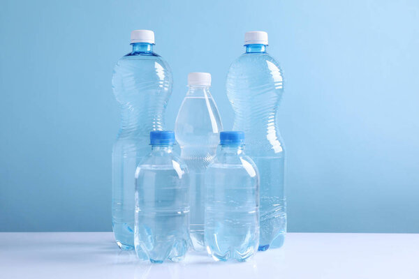 Water bottles of different sizes on white table against light blue background