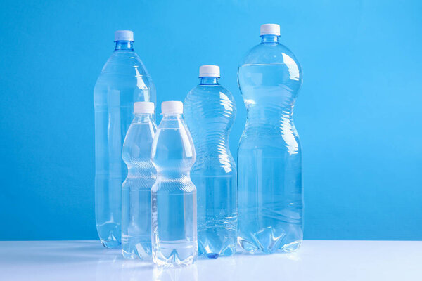 Water bottles of different sizes on white table against light blue background