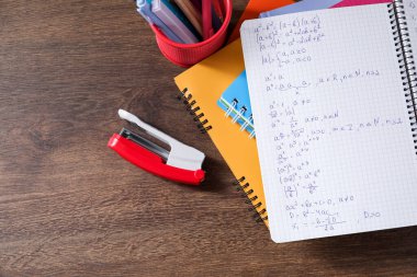Ev ödevi. Matematik formülleri ve ahşap masa üzerindeki farklı kırtasiyelerle dolu defter. Metin için boşluk