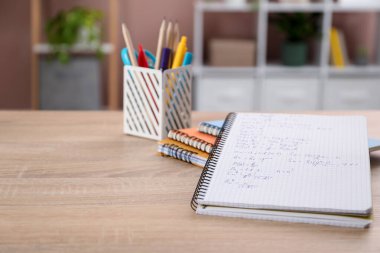 Ev ödevi. Matematik egzersizi ve ahşap masadaki kırtasiyeli defter, yakın plan.