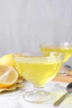 Tatlı kaselerinde leziz sarı jöle ve beyaz mermer masada taze limonlar, yakın plan.