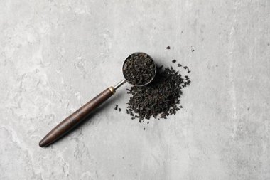 Kurumuş siyah çay yaprakları ve açık gri masada kaşık ölçüsü.