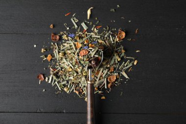 Kurutulmuş bitki çayı yapraklı kepçe siyah ahşap masa, üst manzara.