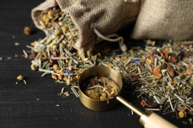 Çuval bezi ve kurutulmuş bitkisel çay yapraklarıyla kaplanmış siyah ahşap masa, yakın plan.