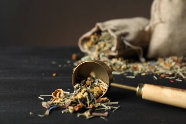 Kurutulmuş bitki çayı yaprakları, kepçe kepçe ve çuval siyah ahşap masa, yakın çekim